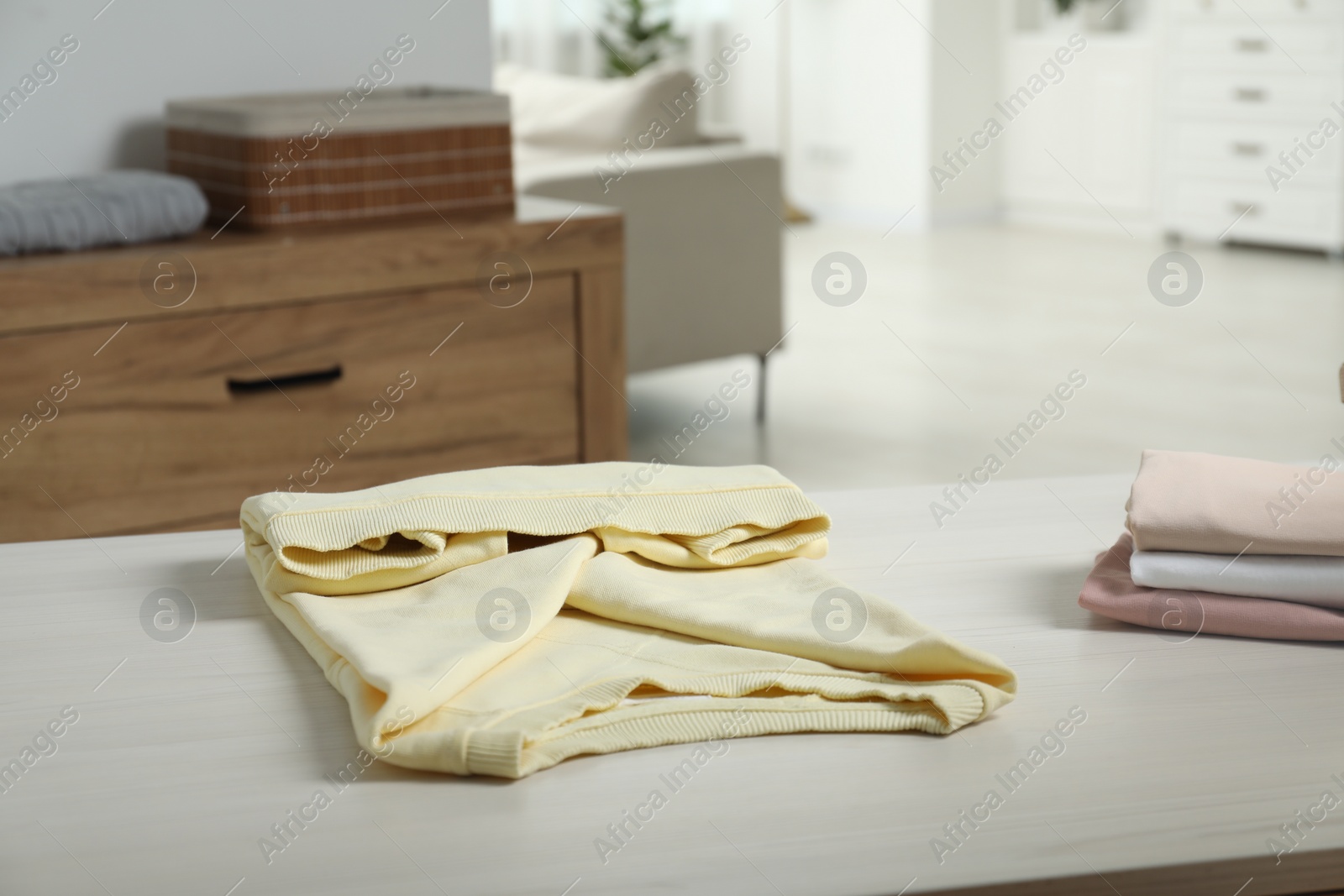 Photo of Different folded clothes on white wooden table at home