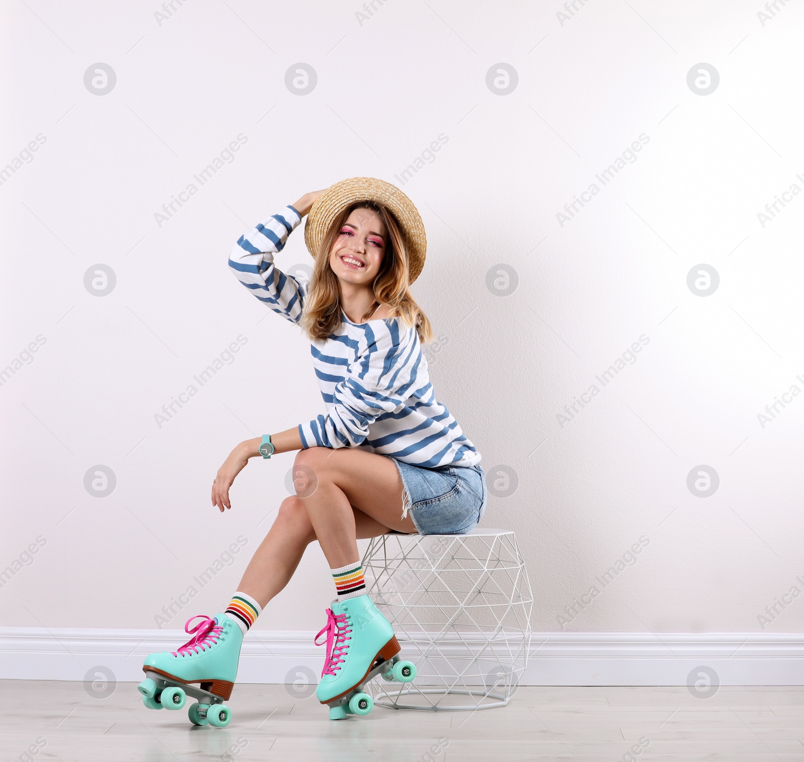 Photo of Young woman with retro roller skates near white wall. Space for text