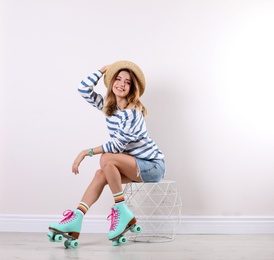 Photo of Young woman with retro roller skates near white wall. Space for text
