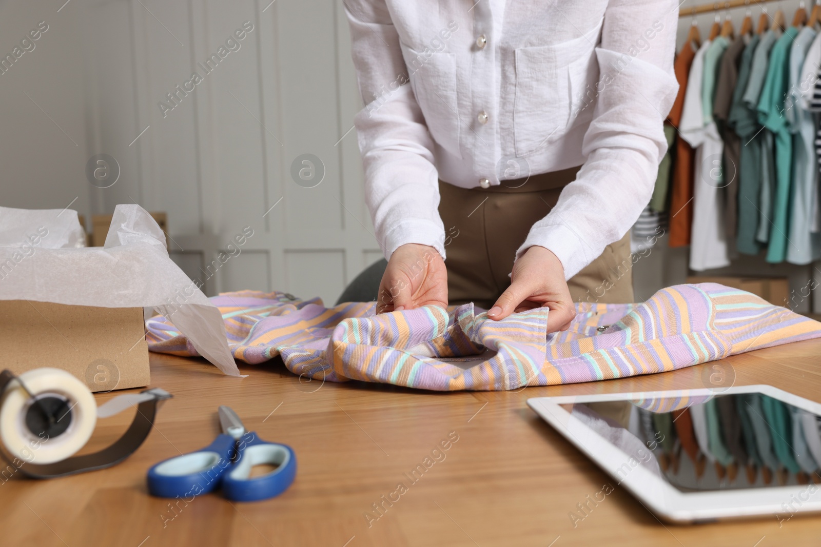 Photo of Seller packing shirt at table in office, closeup. Online store