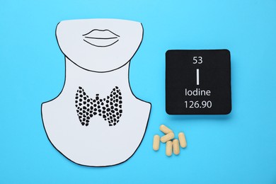 Photo of Card with chemical element Iodine, paper cutout of thyroid gland and pills on light blue background, flat lay