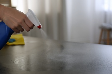 Woman in gloves cleaning grey stone table with rag and detergent indoors, closeup. Space for text