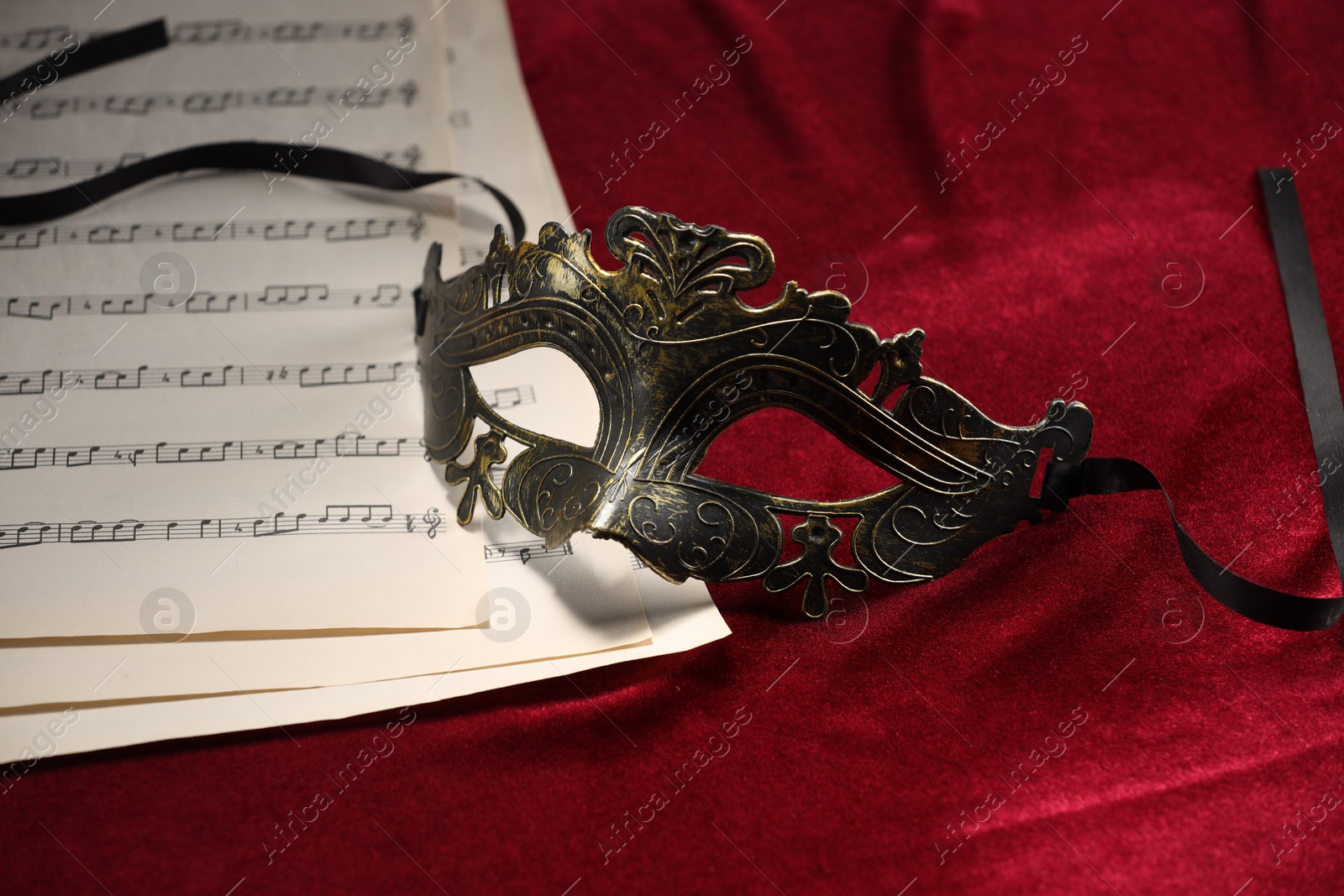 Photo of Elegant face mask and music sheets on red fabric. Theatrical performance