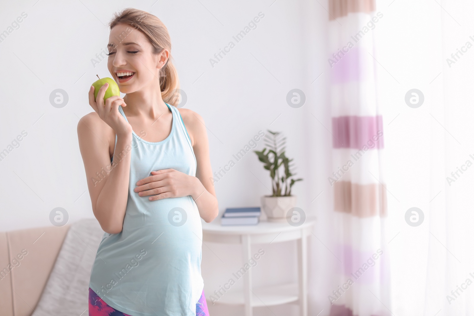 Photo of Young pregnant woman eating apple at home