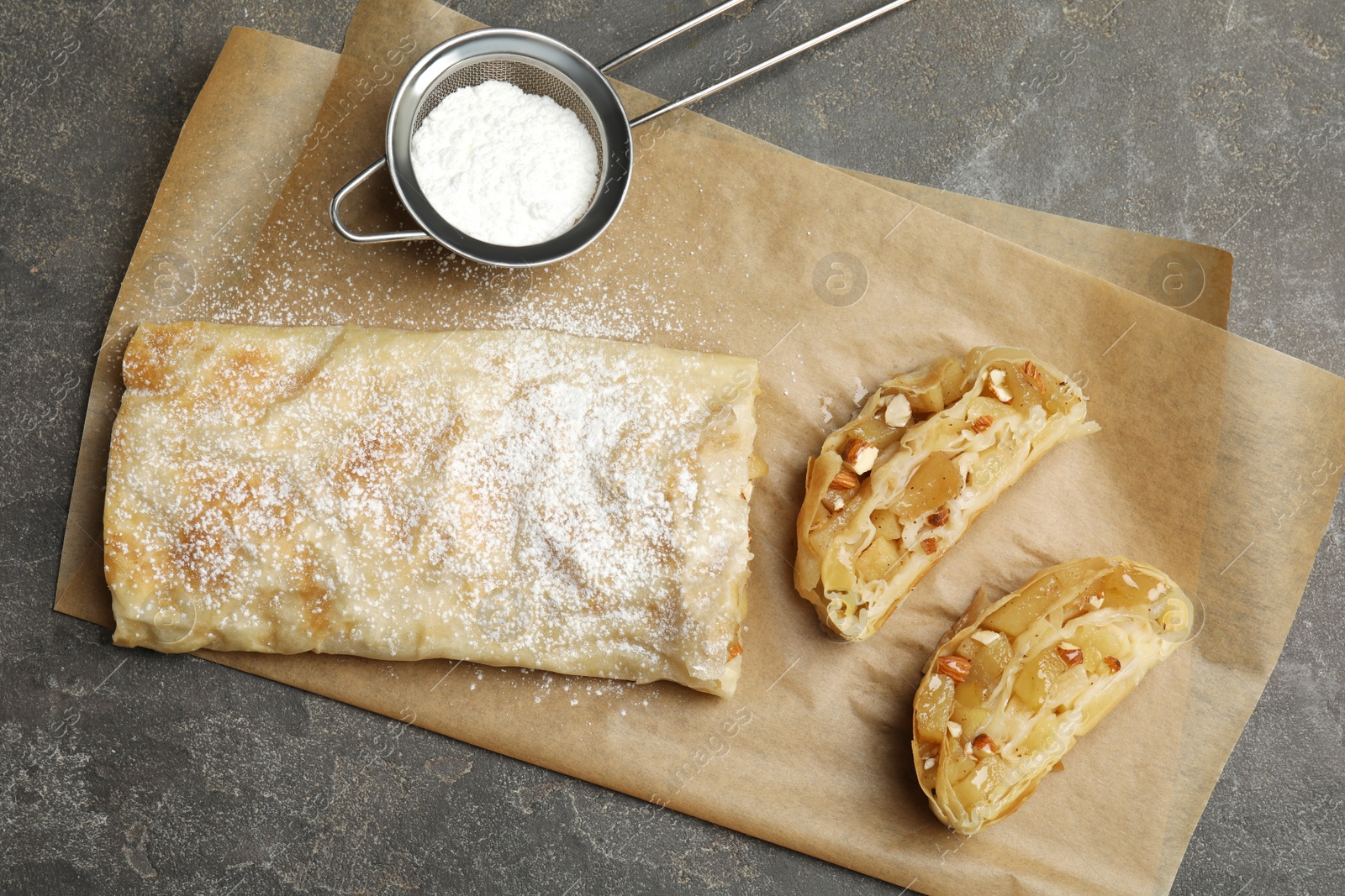 Photo of Delicious apple strudel with almonds and powdered sugar on grey table, flat lay