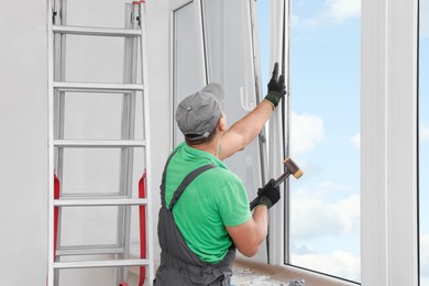 Worker in uniform installing double glazing window indoors