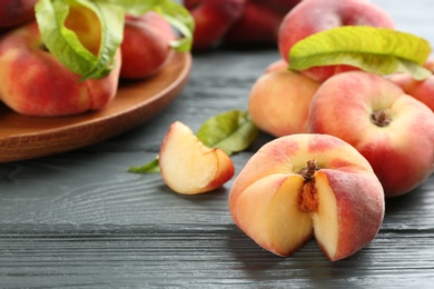 Photo of Fresh ripe donut peaches on grey wooden table, closeup. Space for text