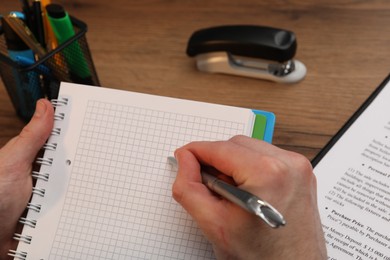 Photo of Man taking notes at wooden table, closeup