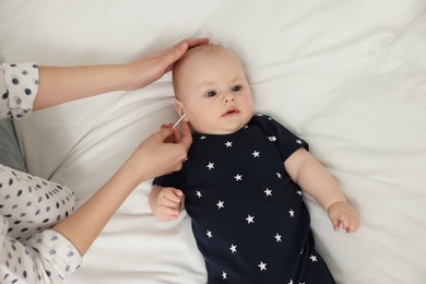 Photo of Mother cleaning ears of her baby with cotton bud on bed, top view