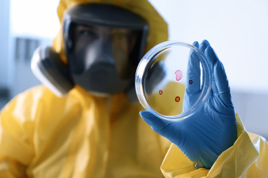 Scientist in chemical protective suit with Petri dish at laboratory, focus on hand. Virus research