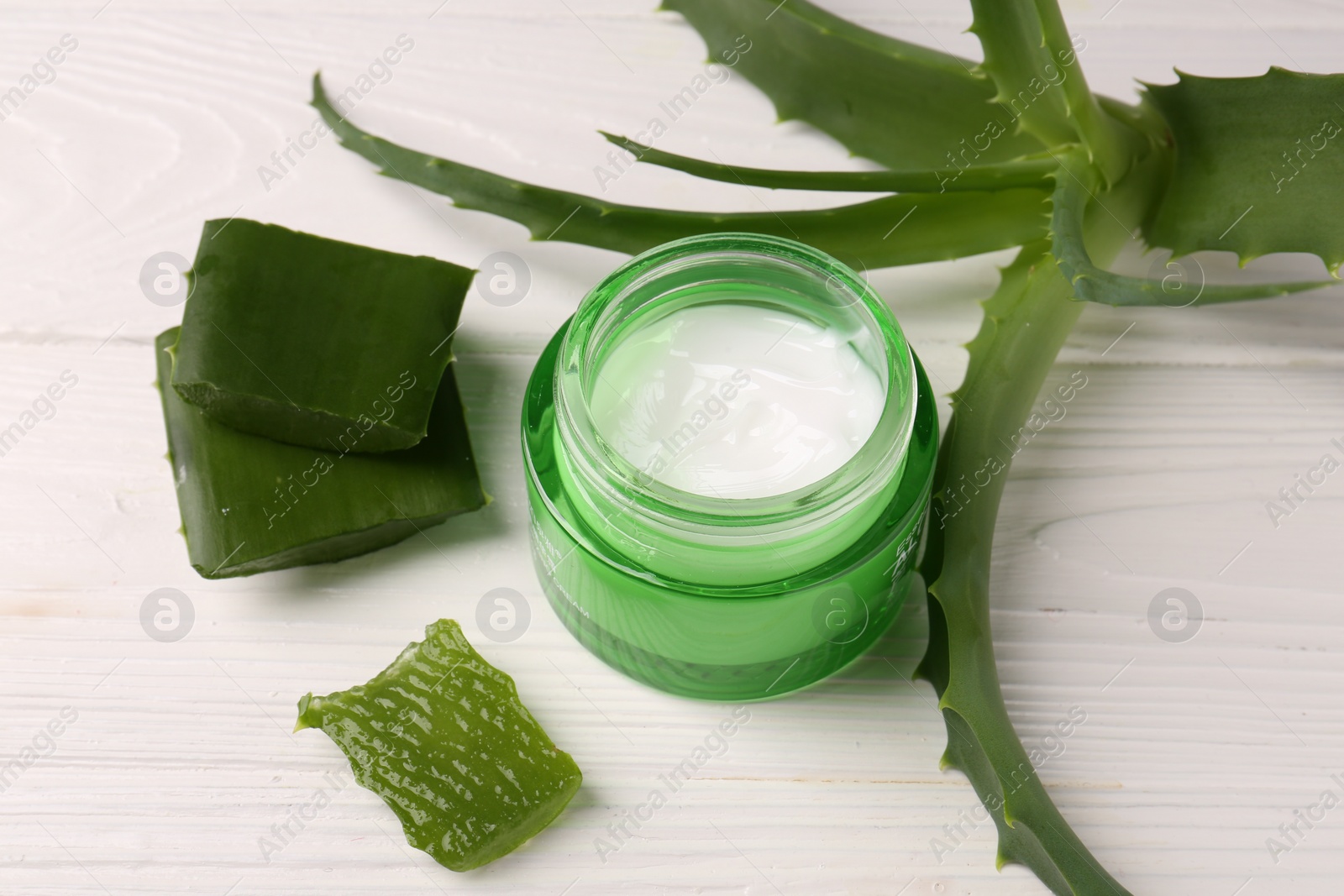 Photo of Jar of cosmetic cream and aloe vera leaves on white wooden table