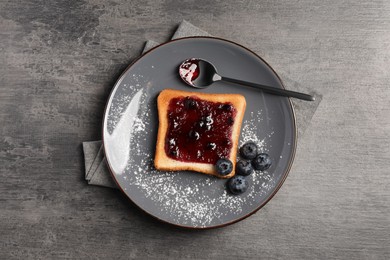 Photo of Delicious toast served with jam and blueberries on grey wooden table, top view