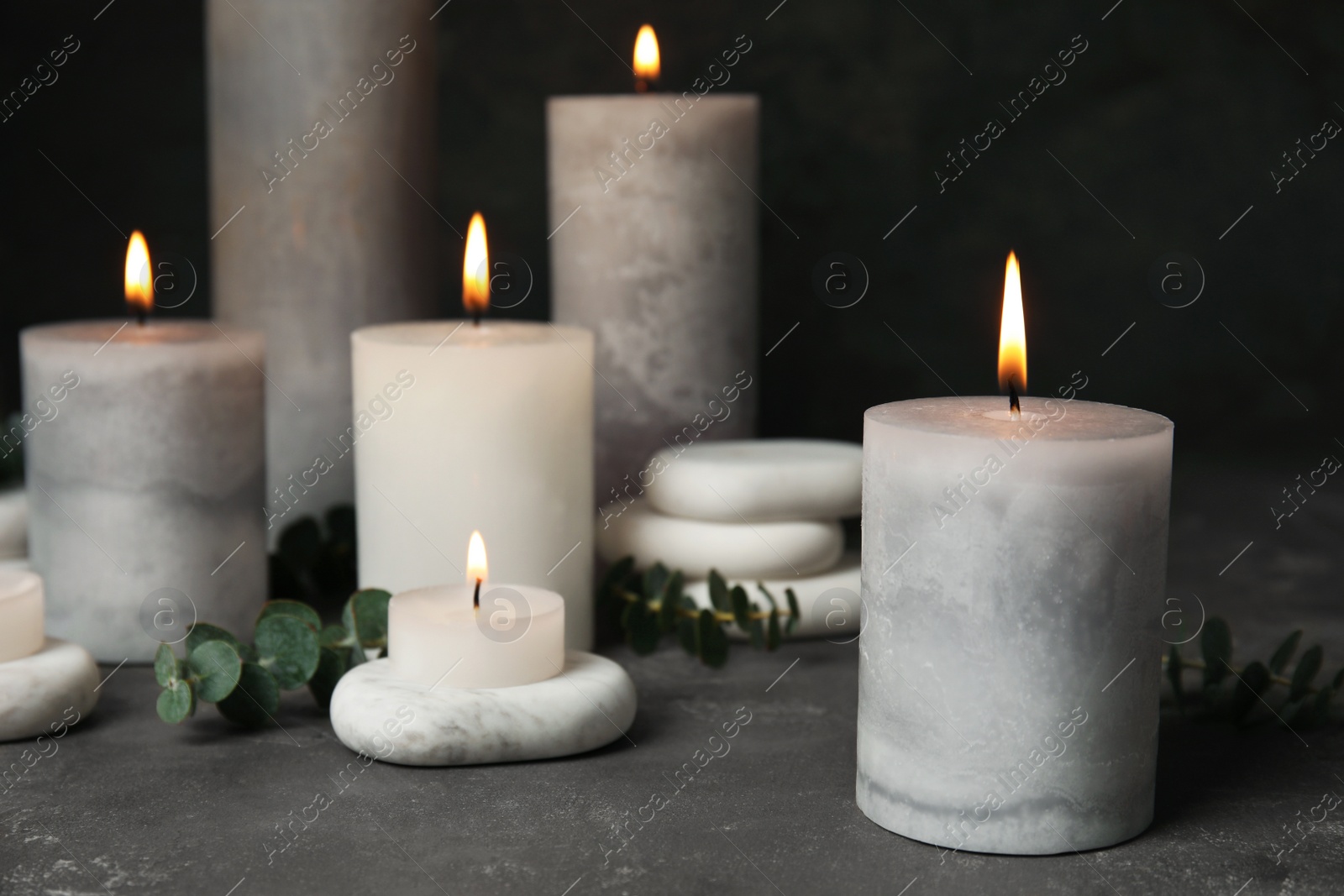 Photo of Composition with burning candles, spa stones and eucalyptus on grey table