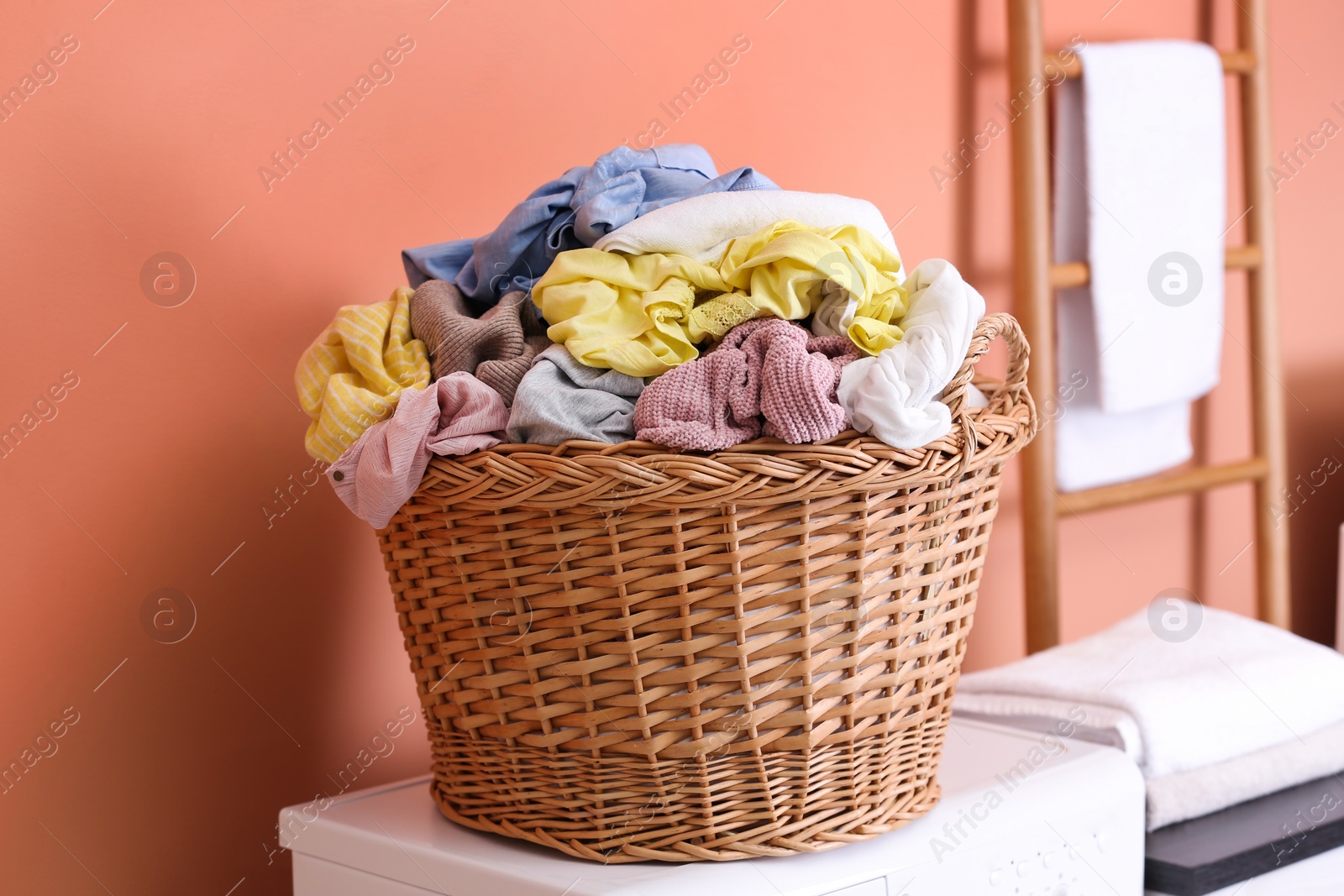 Photo of Wicker basket with dirty laundry on washing machine near coral wall indoors