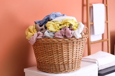 Wicker basket with dirty laundry on washing machine near coral wall indoors