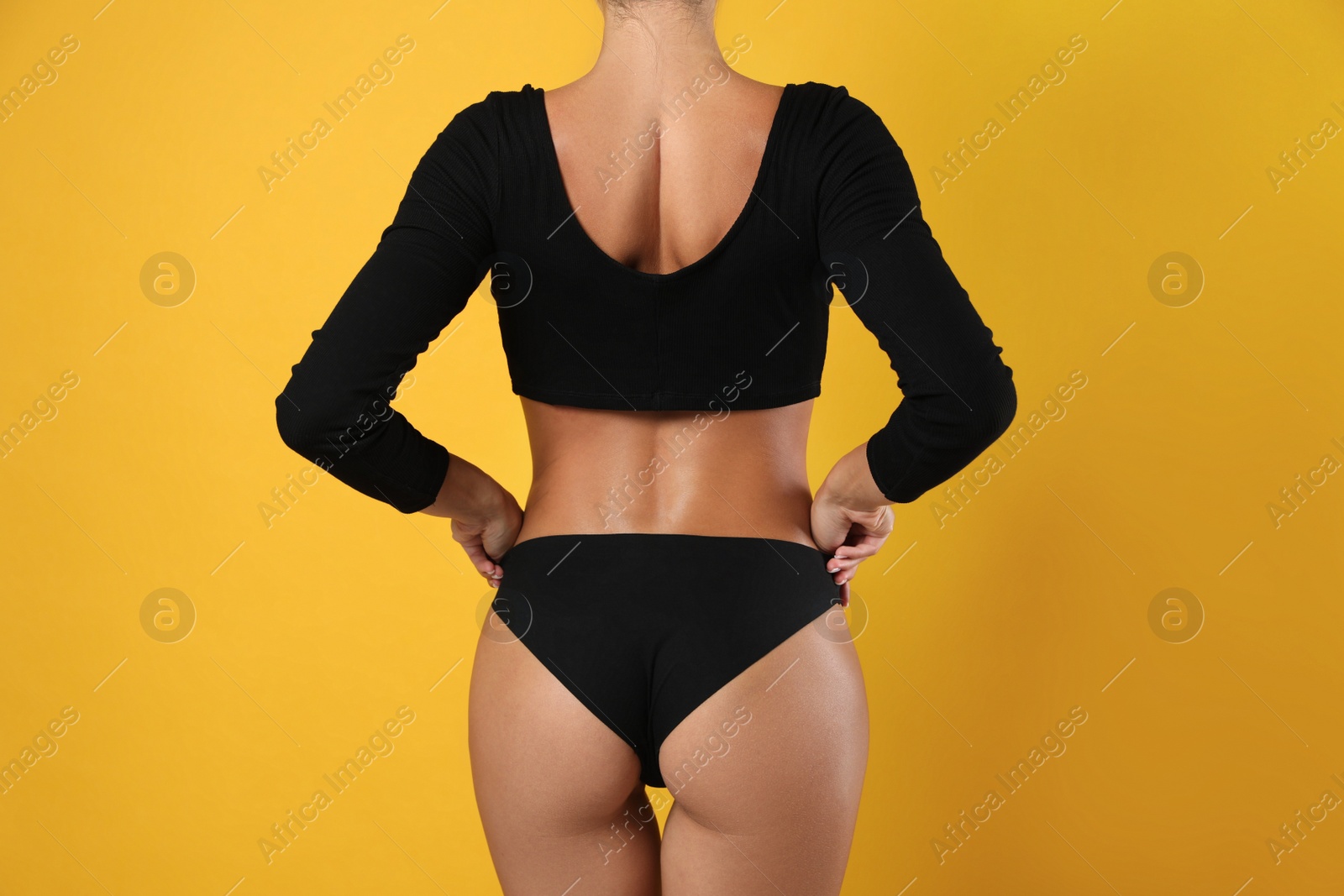 Photo of Woman in black sexy panties on yellow background, closeup