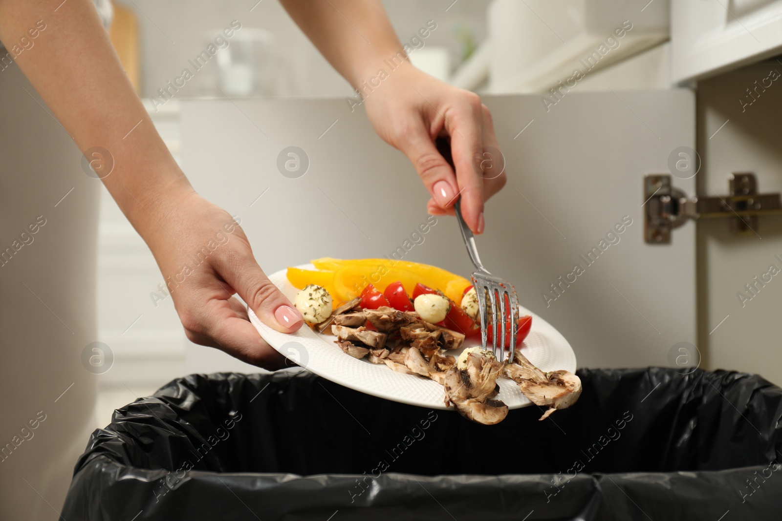 Photo of Woman throwing vegetable and mushrooms into bin indoors, closeup