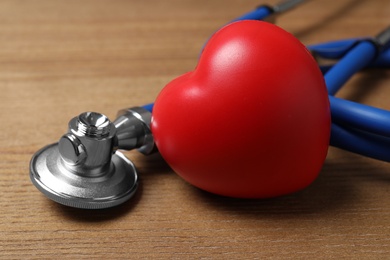 Photo of Red heart with stethoscope on wooden background, closeup