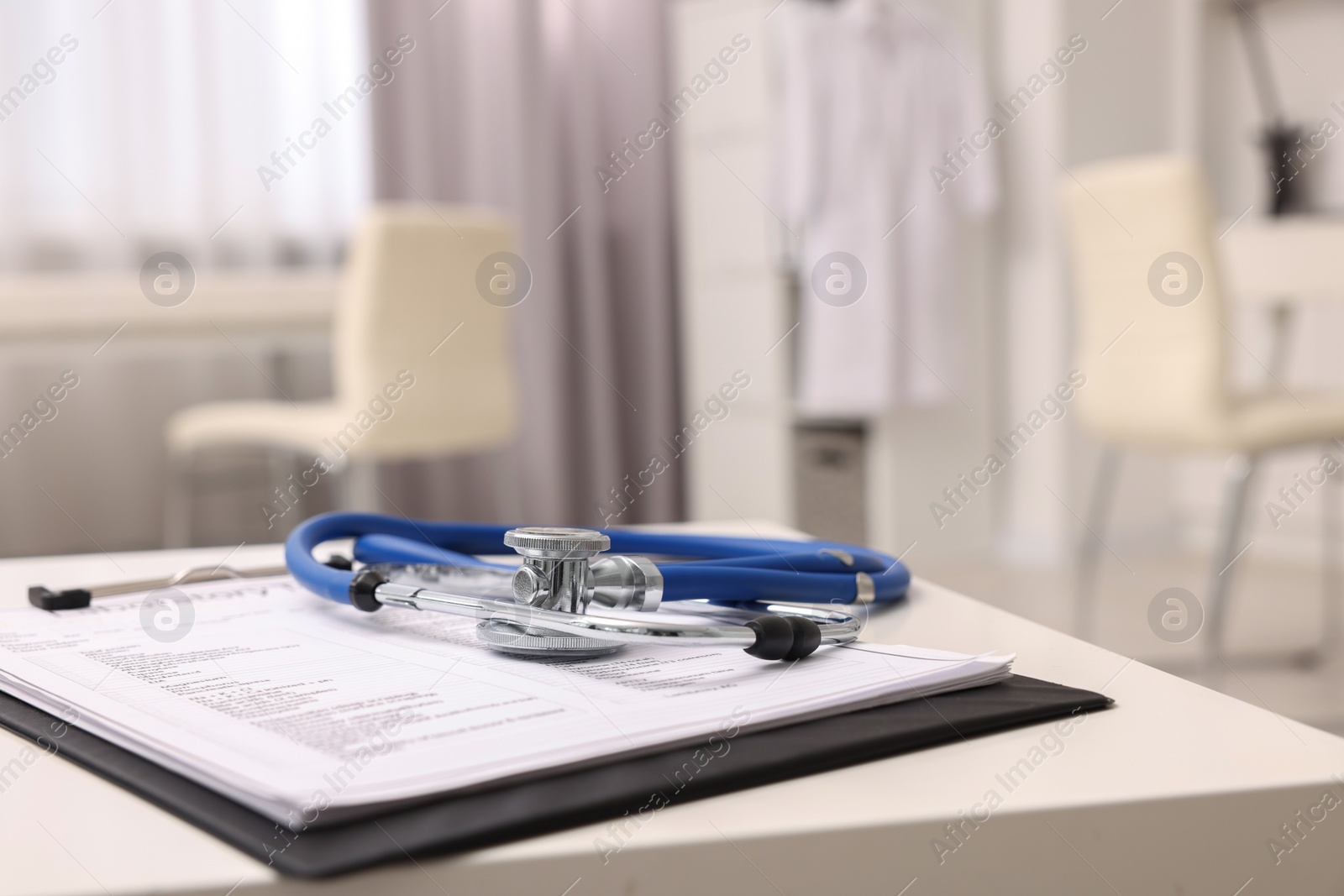 Photo of Clipboard and stethoscope on white table in clinic, space for text. Doctor's workplace