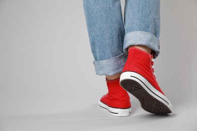 Photo of Woman wearing pair of new stylish sneakers on light grey background, closeup. Space for text