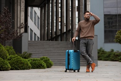 Photo of Being late. Worried man with suitcase near building outdoors, space for text