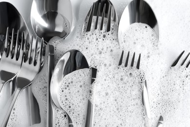 Photo of Many forks and spoons in foam, flat lay. Washing silverware