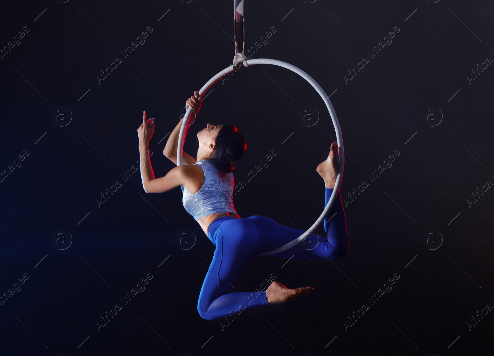 Photo of Young woman performing acrobatic element on aerial ring indoors