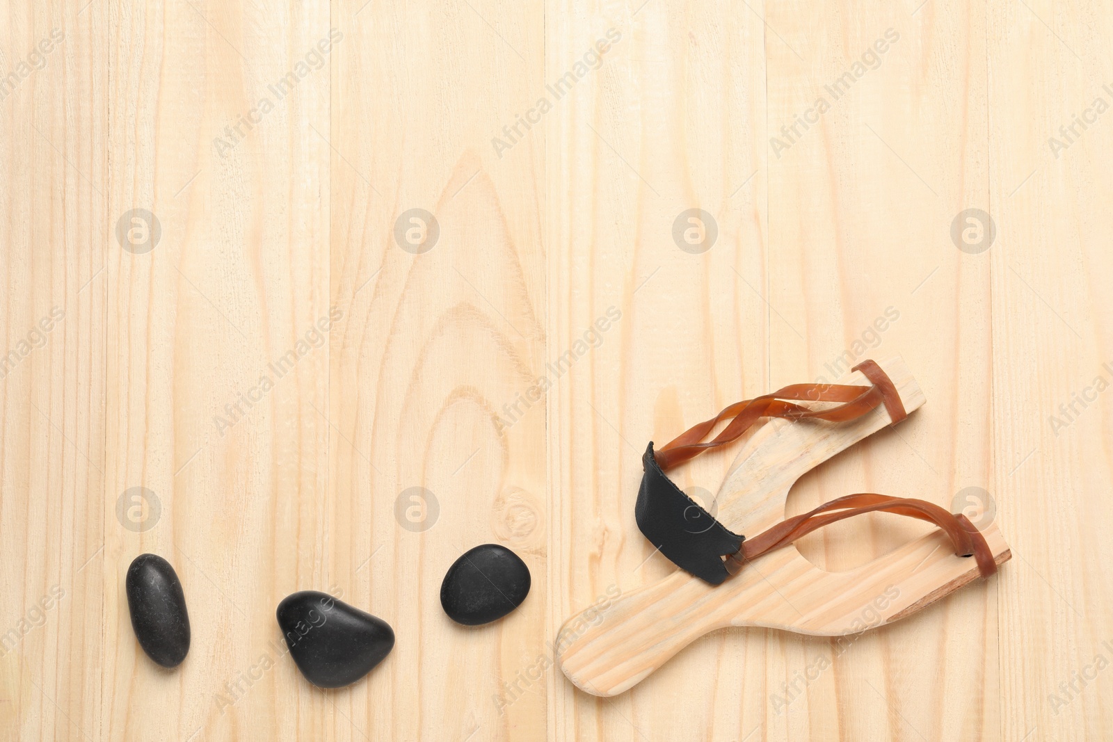 Photo of Slingshot with stones on wooden background, flat lay. Space for text