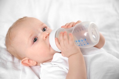 Baby drinking milk from bottle on bed, closeup