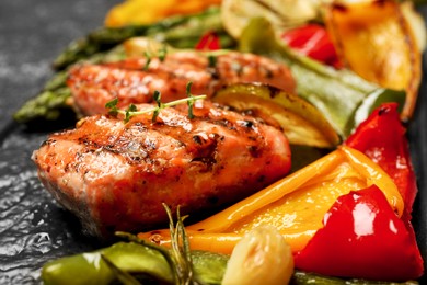 Photo of Tasty grilled salmon with vegetables on black slate, closeup