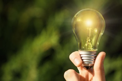 Image of Woman holding glowing light bulb outdoors, closeup. Space for text