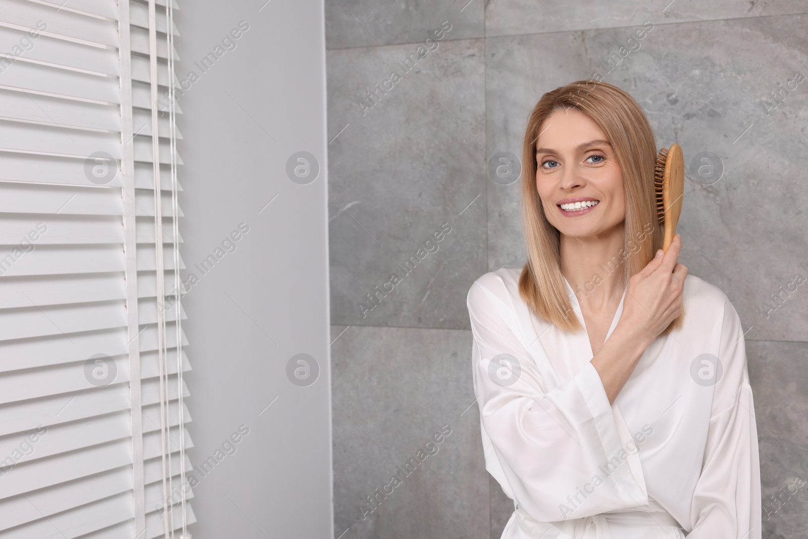 Photo of Beautiful woman brushing her hair in bathroom. Space for text