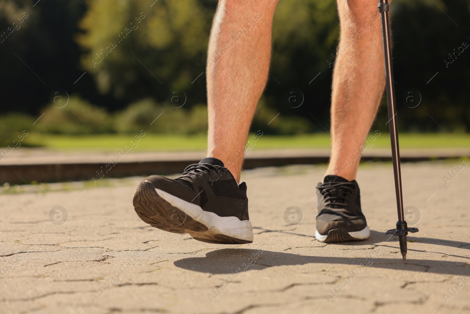 Photo of Man practicing Nordic walking with poles outdoors on sunny day, closeup