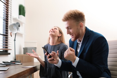 Photo of Happy young people playing online lottery using smartphone in office