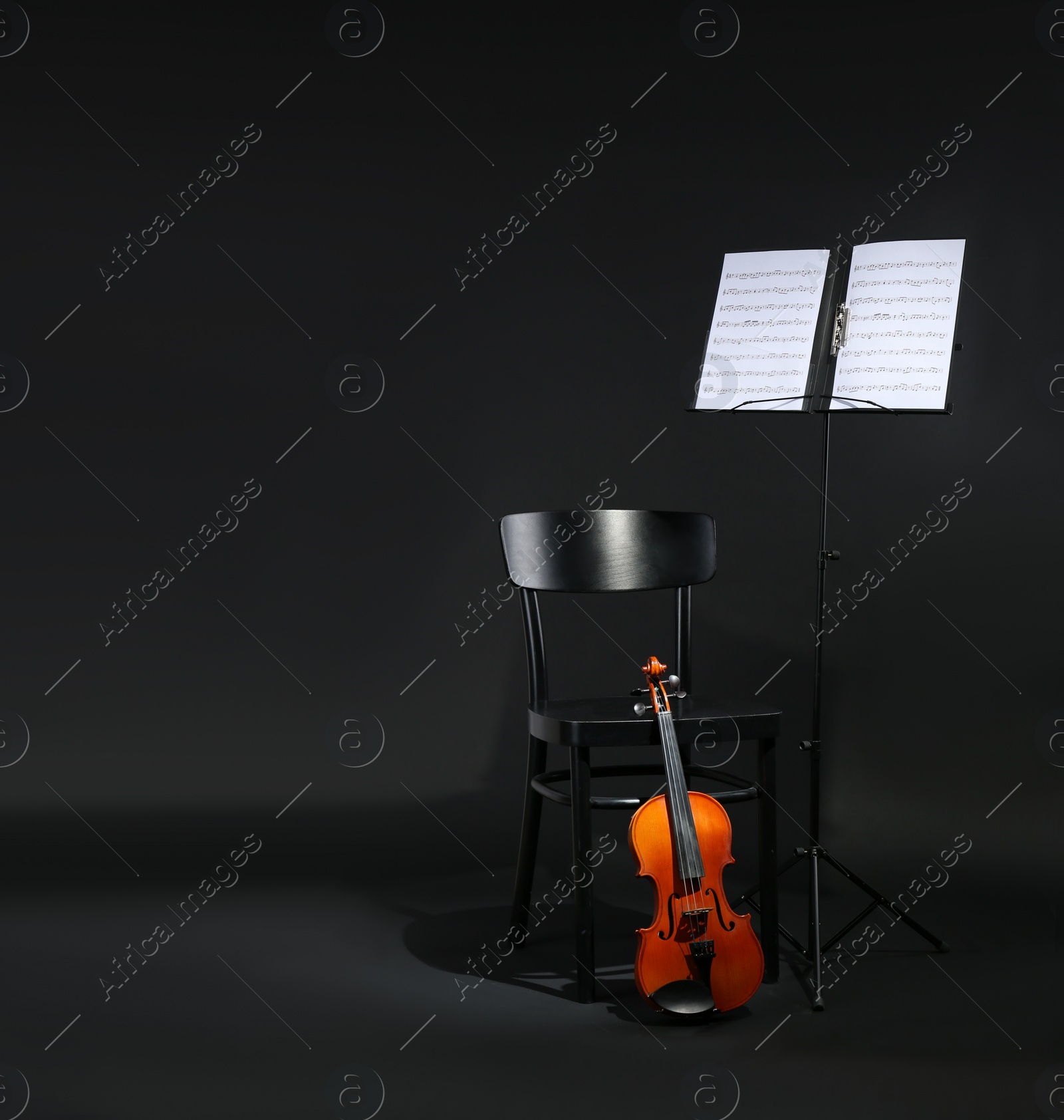 Photo of Violin, chair and note stand with music sheets on black background. Space for text