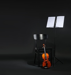 Photo of Violin, chair and note stand with music sheets on black background. Space for text