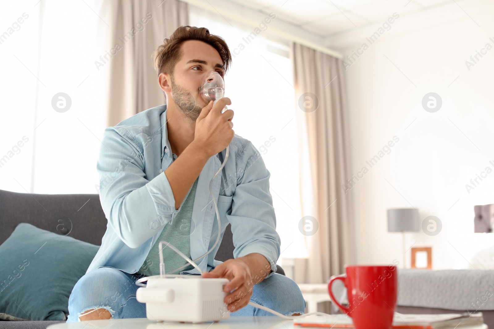 Photo of Young man using asthma machine at home. Space for text