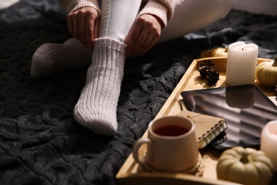 Photo of Woman in warm socks relaxing with cup of hot drink on knitted plaid, closeup