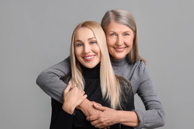 Family portrait of young woman and her mother on grey background