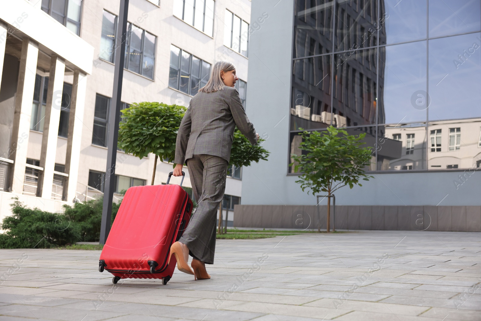 Photo of Being late. Senior businesswoman with red suitcase running outdoors, low angle view