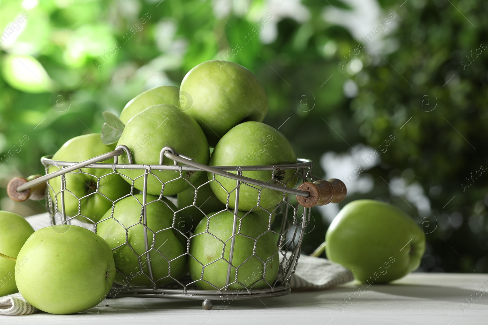 Photo of Metal basket with ripe green apples on white table outdoors. Space for text