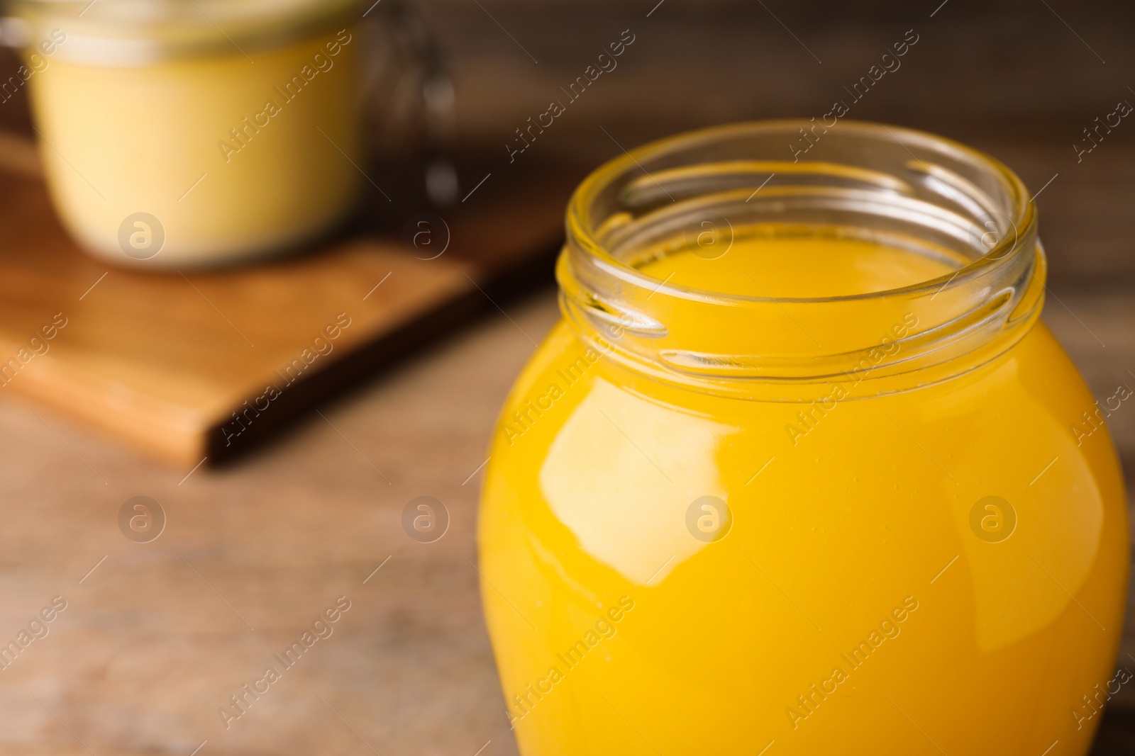 Photo of Glass jar of Ghee butter on wooden table, closeup. Space for text