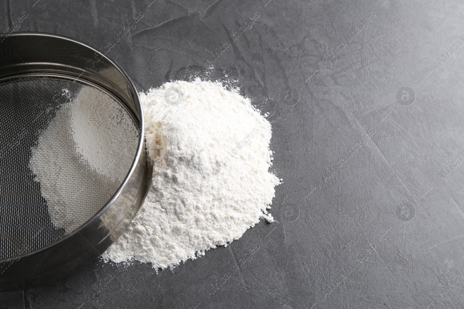 Photo of Metal sieve and flour on grey table. Space for text