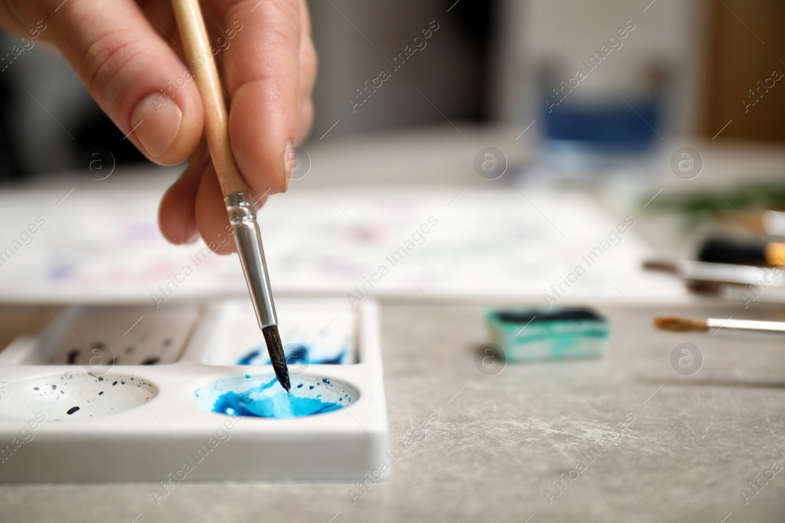 Photo of Woman painting with watercolor at grey stone table, closeup. Space for text