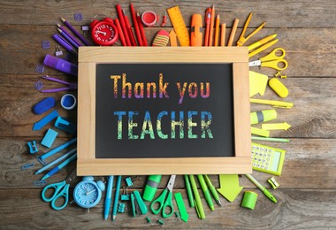 Small blackboard with phrase Thank You Teacher and different colorful stationery on wooden table, flat lay