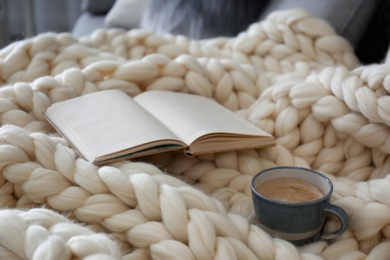 Photo of Cup of coffee and book on white knitted plaid indoors