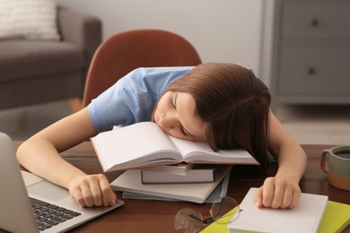 Photo of Young tired woman sleeping near books at wooden table indoors