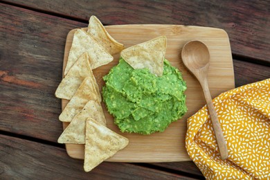 Photo of Delicious guacamole made of avocados, nachos and spoon on wooden table, flat lay