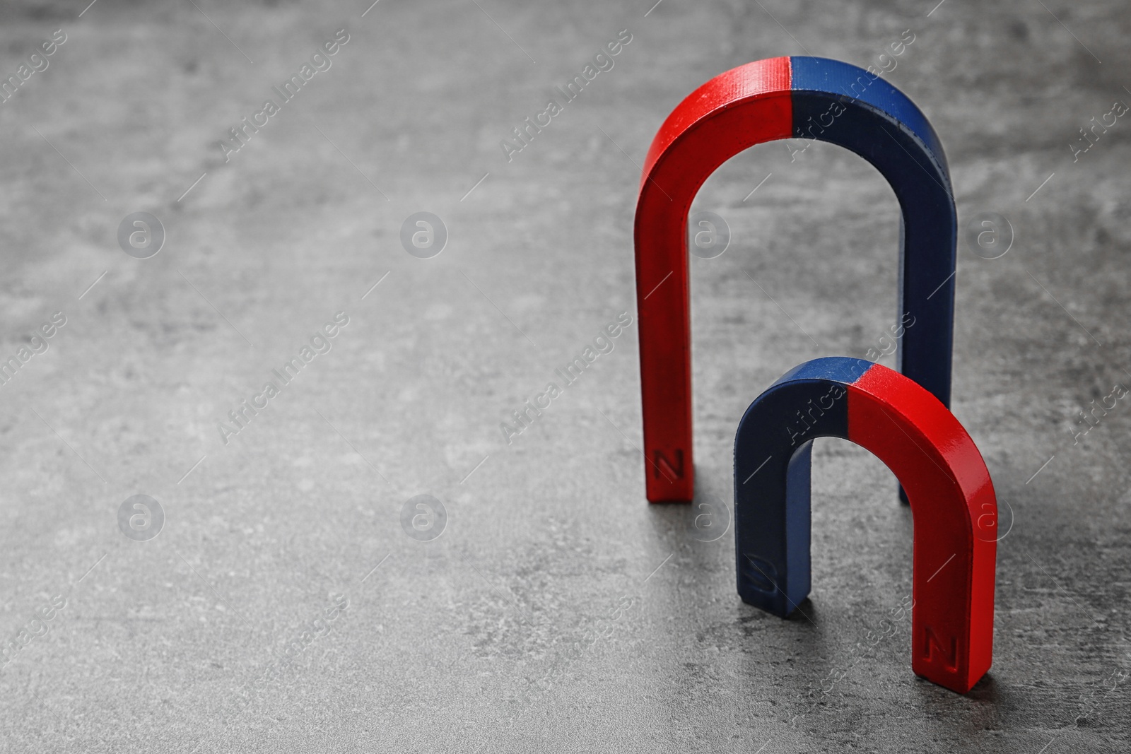 Photo of Red and blue horseshoe magnets on grey background. Space for text