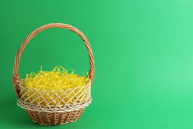 Photo of Easter basket with yellow paper filler on green background, space for text